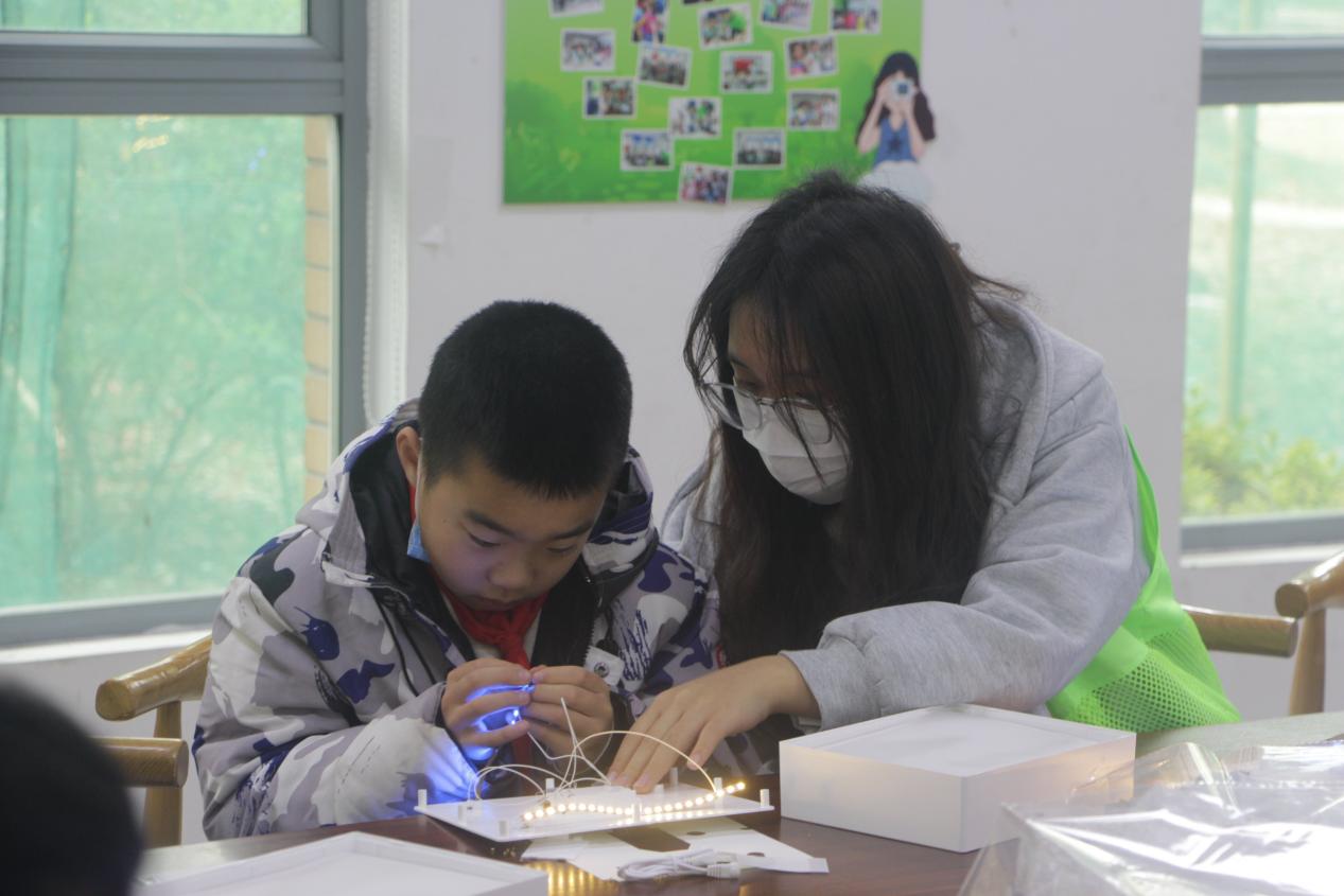 图为志愿者帮助小朋友制作纸雕